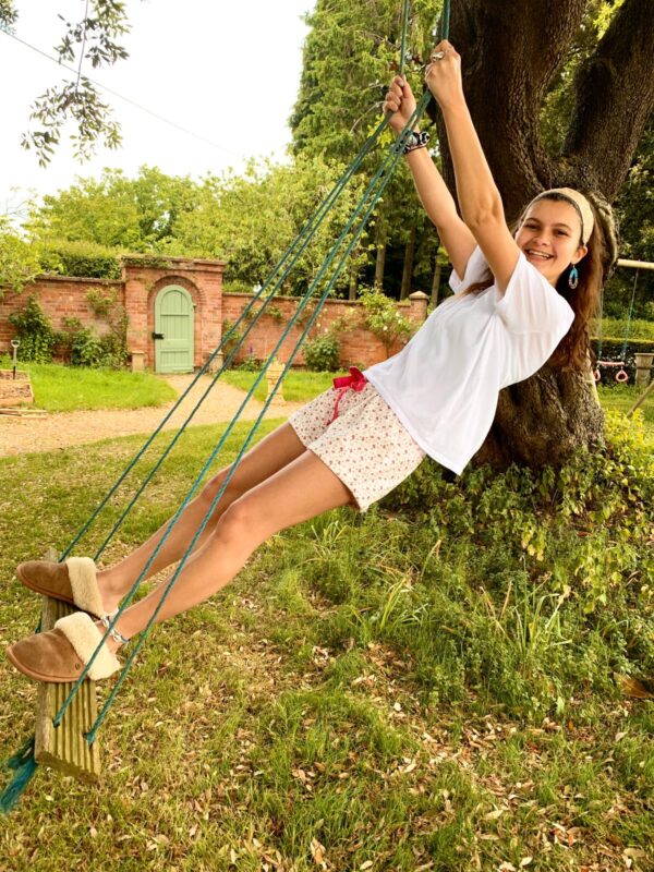 Molly on a swing under a tree wearing strawberry print brushed cotton Pyjama House sleep shorts with drawstring tie